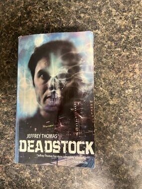 Deadstock by Jeffrey Thomas — Sci‑Fi Horror Paperback (Black, Blue, Purple)